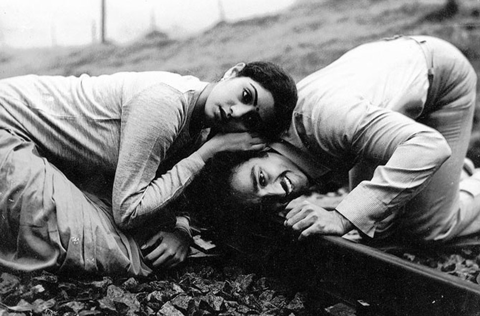 Kamal Haasan and Sridevi lying together on railway ballast in black and white, her head resting against his